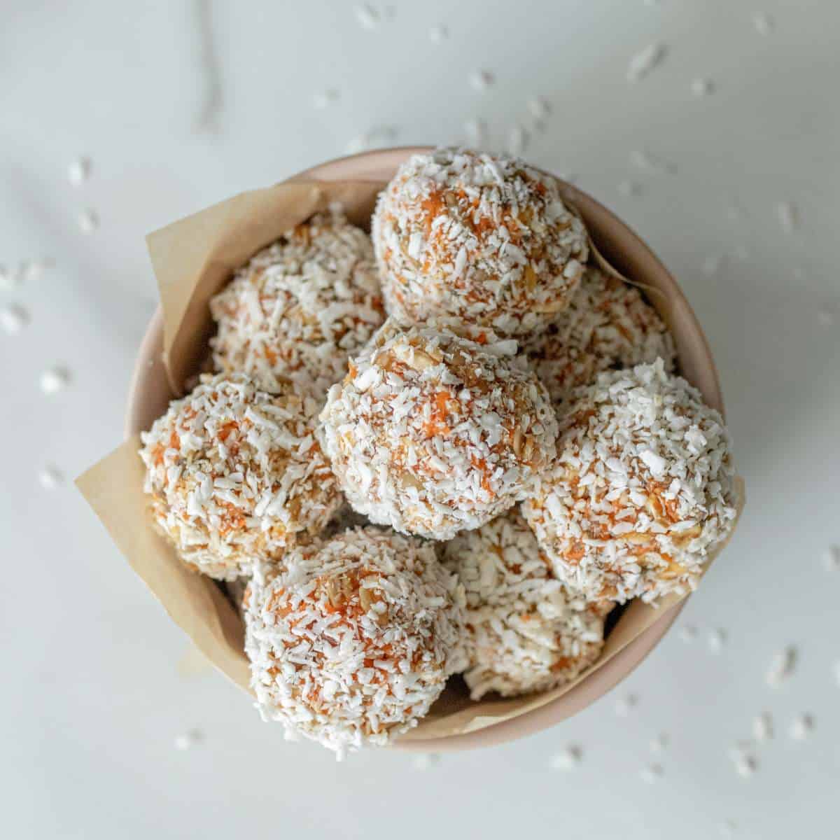 Completed carrot cake energy balls covered in shredded coconut in a small bowl on a countertop.