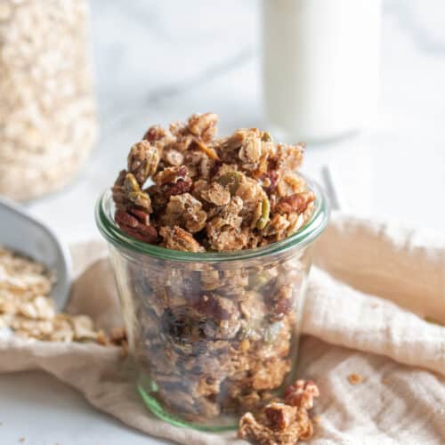 Egg white granola in a jar, on a staged table top with granola around.