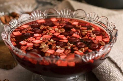 a decorative crystal bowl with black cherry jello salad topped with cream cheese and pecans