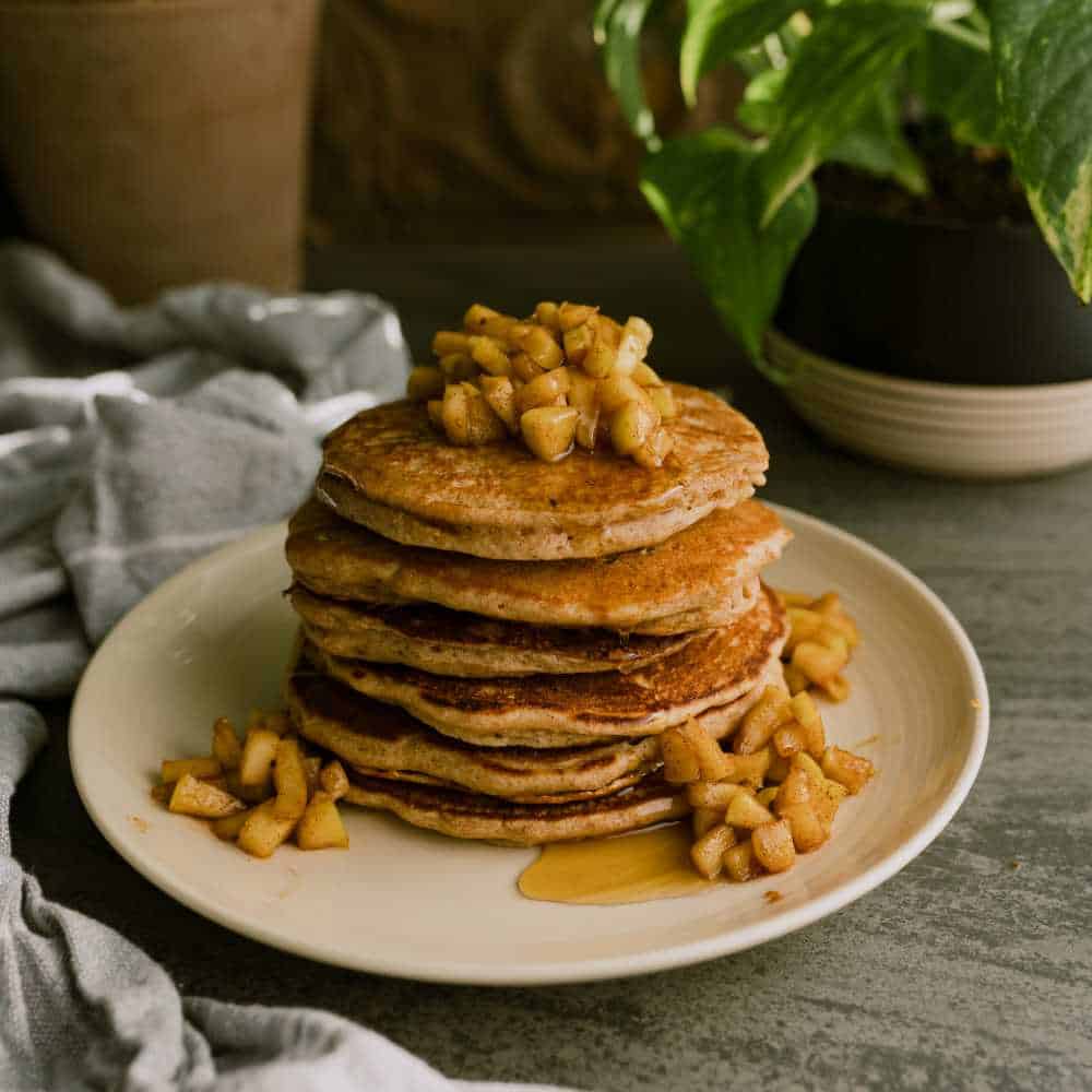 stack of spelt pancakes topped with apple cinnamon topping with a drizzle of maple syrup