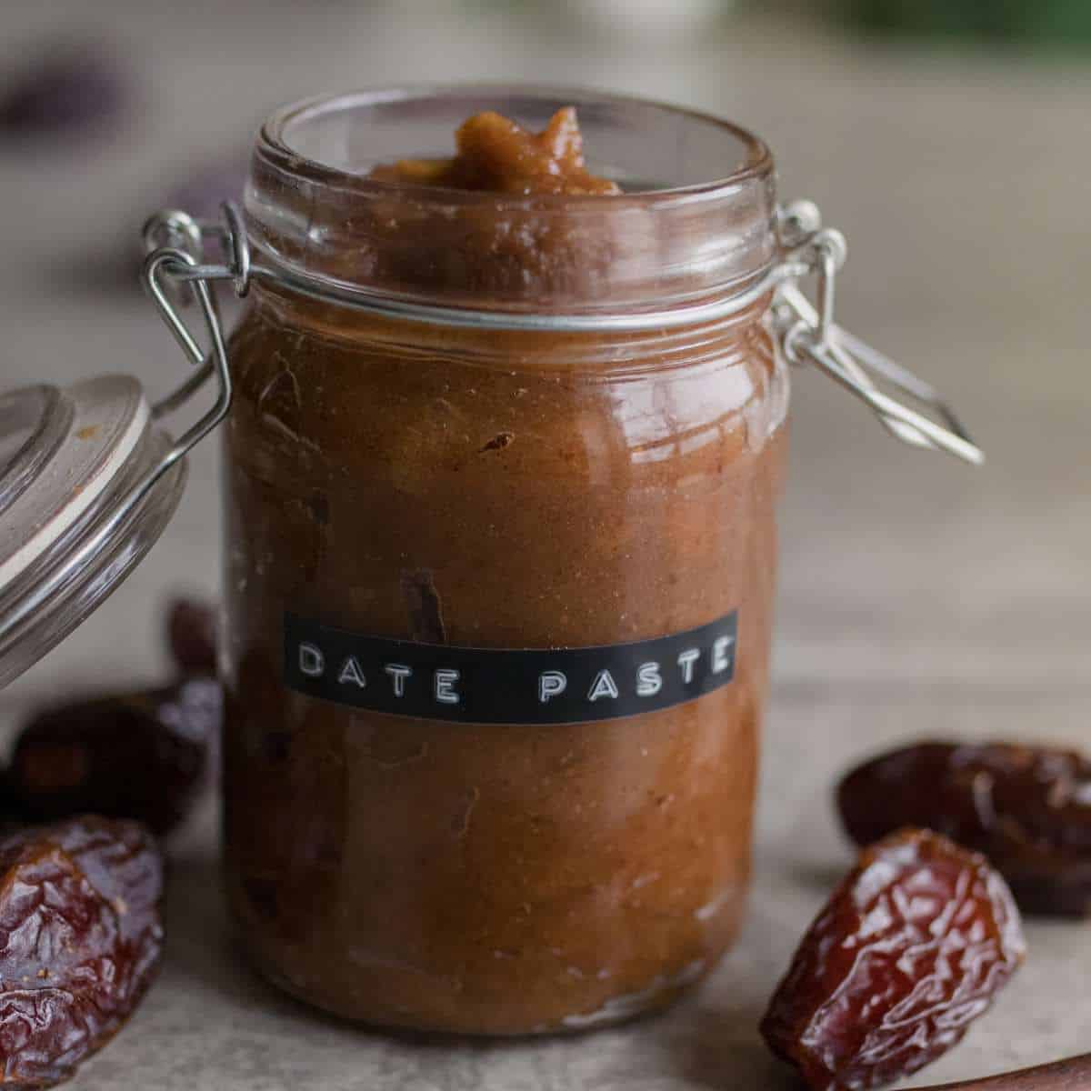 a glass jar filled with date paste sitting on a table with the words date paste written on the jar and a few dates sitting on the table beside the jar.