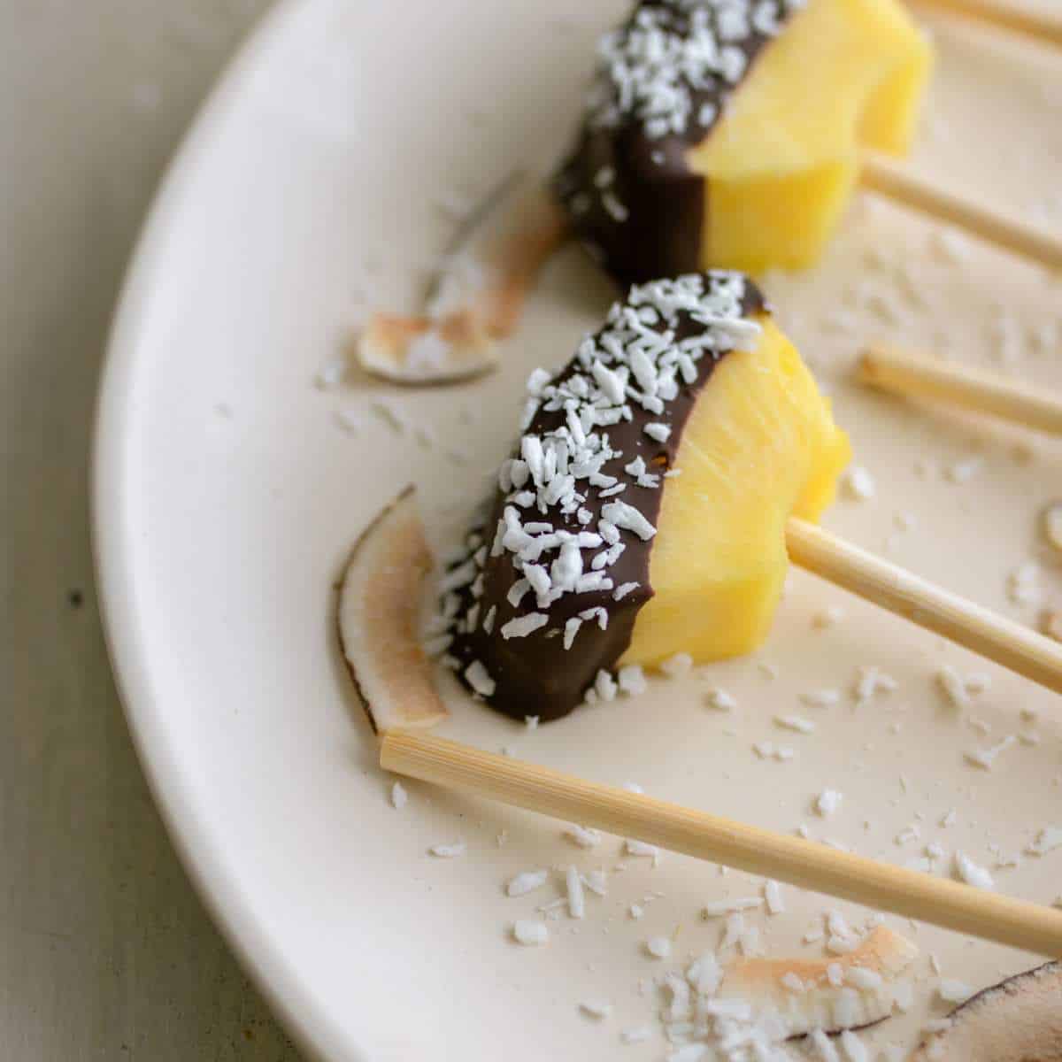 Chocolate covered pineapples with shredded coconut on a plate.