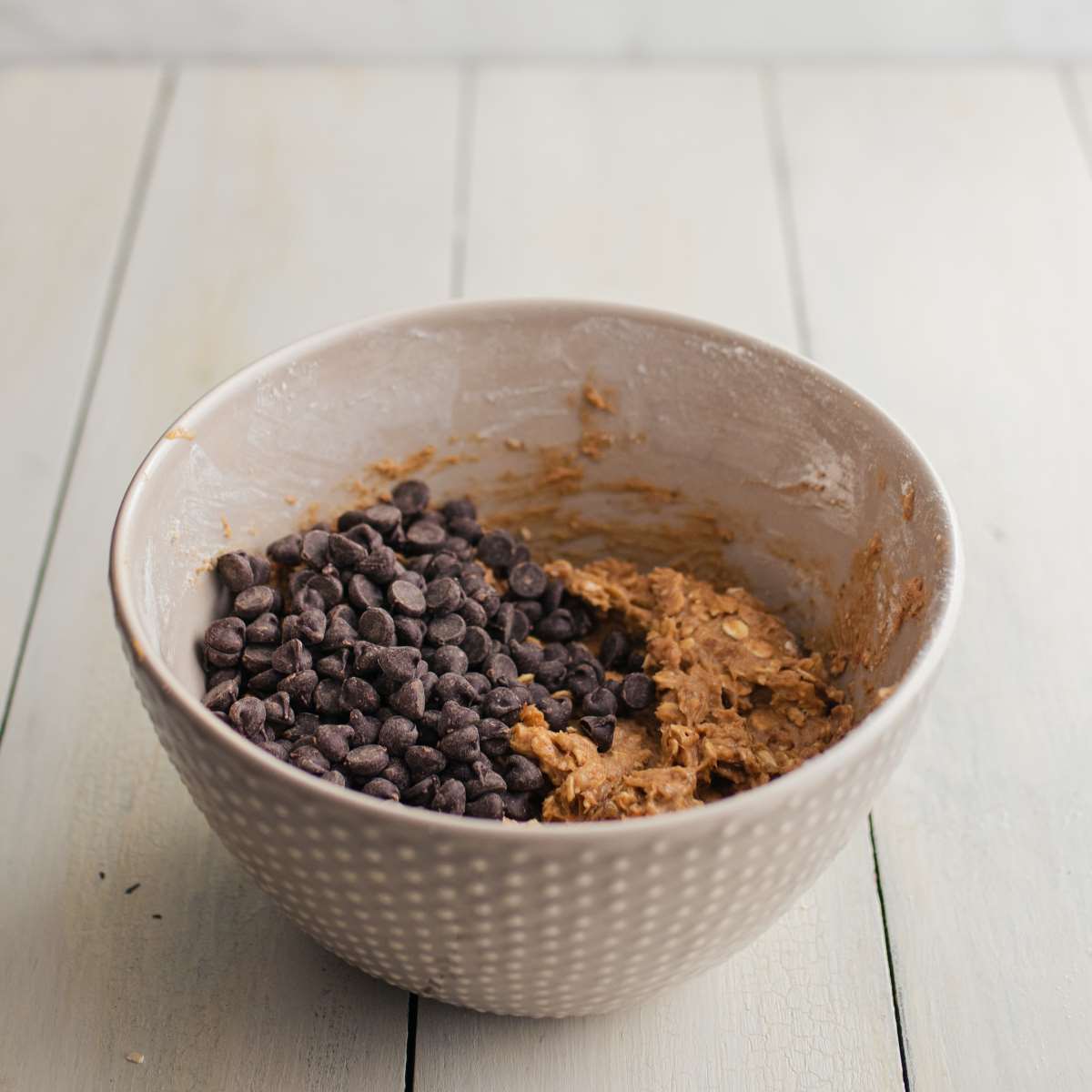 Chocolate chips sitting on top cookie dough in a mixing bowl.