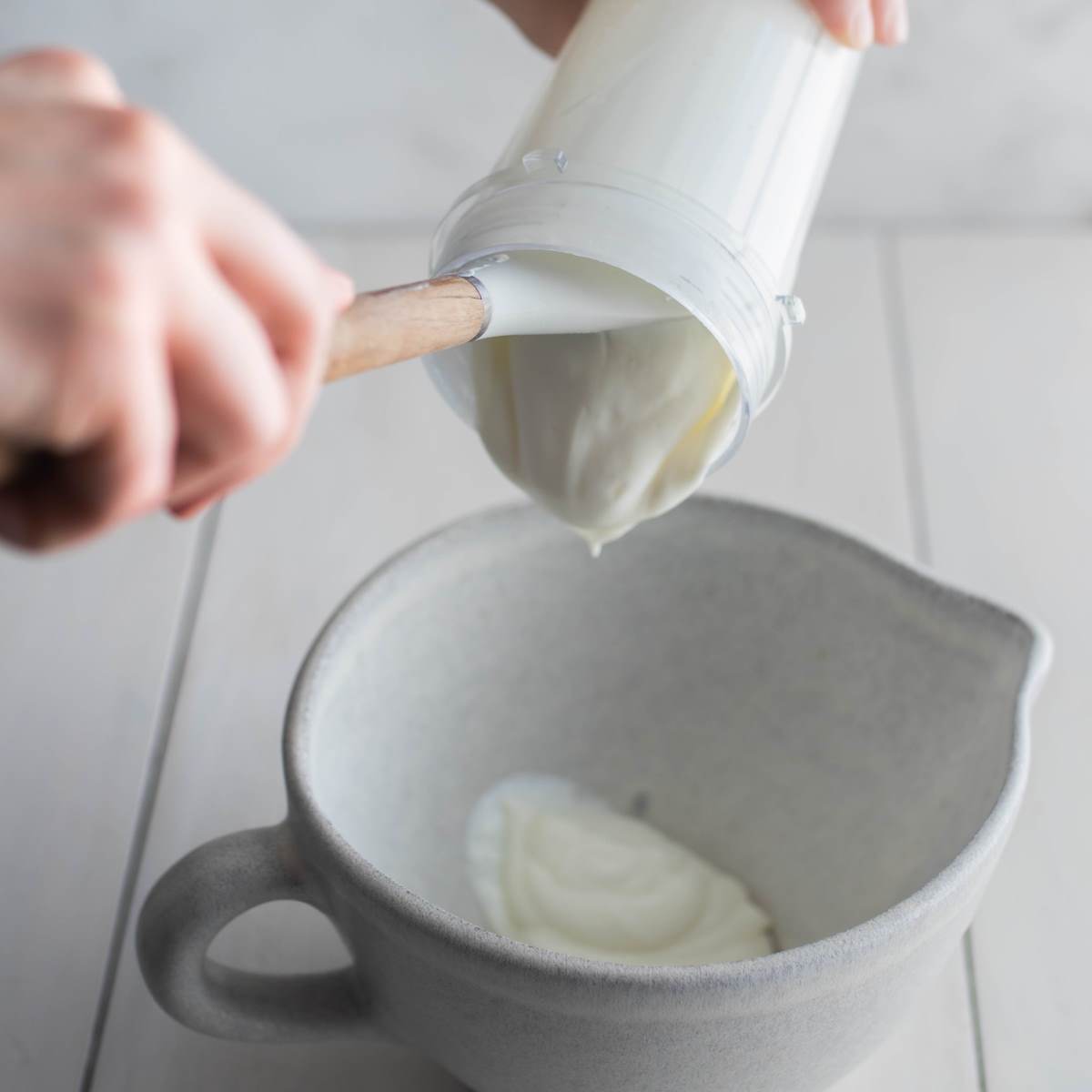 Blended cottage cheese being scooped out of a blender cup with a spatula into a mixing bowl.