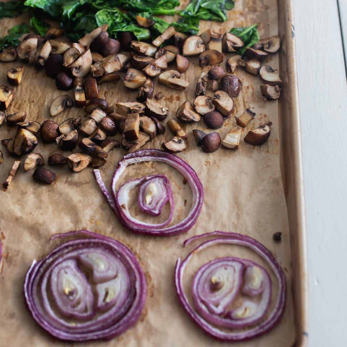 Oven-roasted mushroom, onion and spinach drizzled with olive oil on a baking sheet.