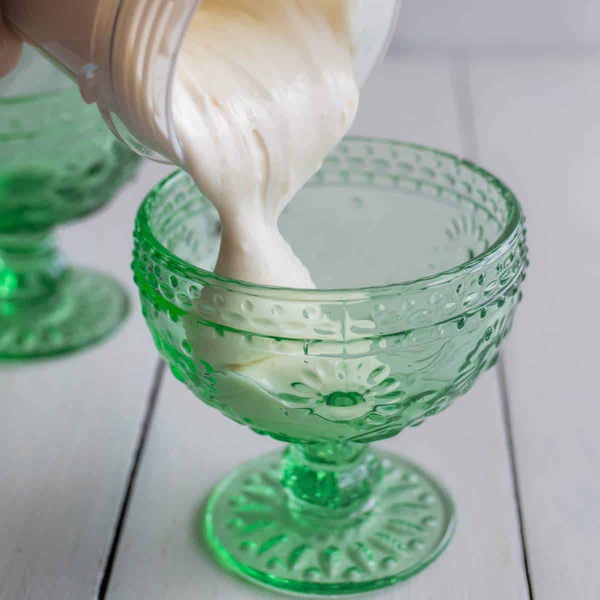 Pouring Cottage Cheese Lemon Mousse from a blender cup into a green dessert bowl.
