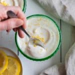 Green, dessert bowl full of Cottage Cheese Lemon Mousse on a wooden board with a handle spooning a scoop out.