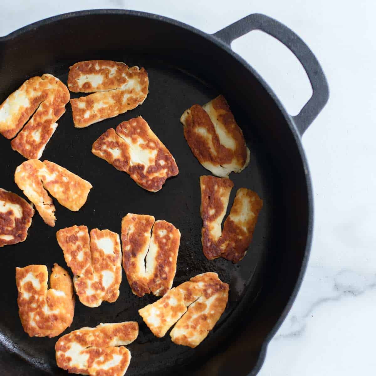 Fried halloumi cheese strips in a cast iron skillet. 