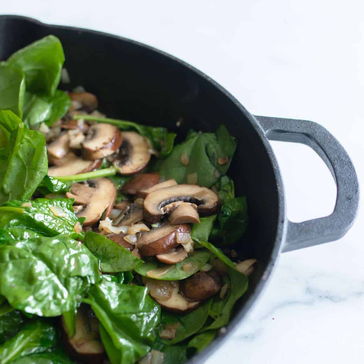 Sautéing spinach in a cast iron pan with mushroom and onion.