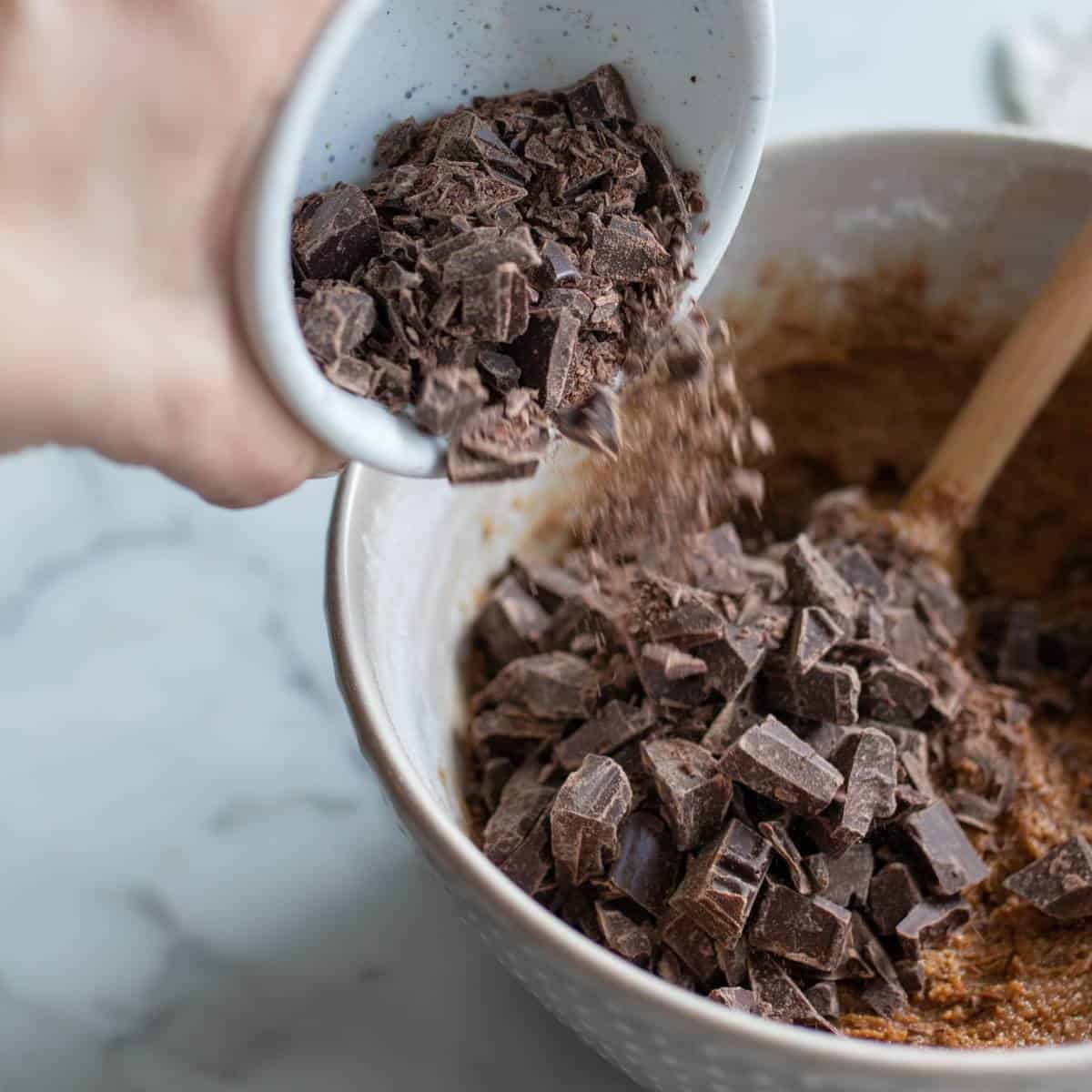 Chocolate chunks falling into spelt cookie dough from small mixing bowl. 
