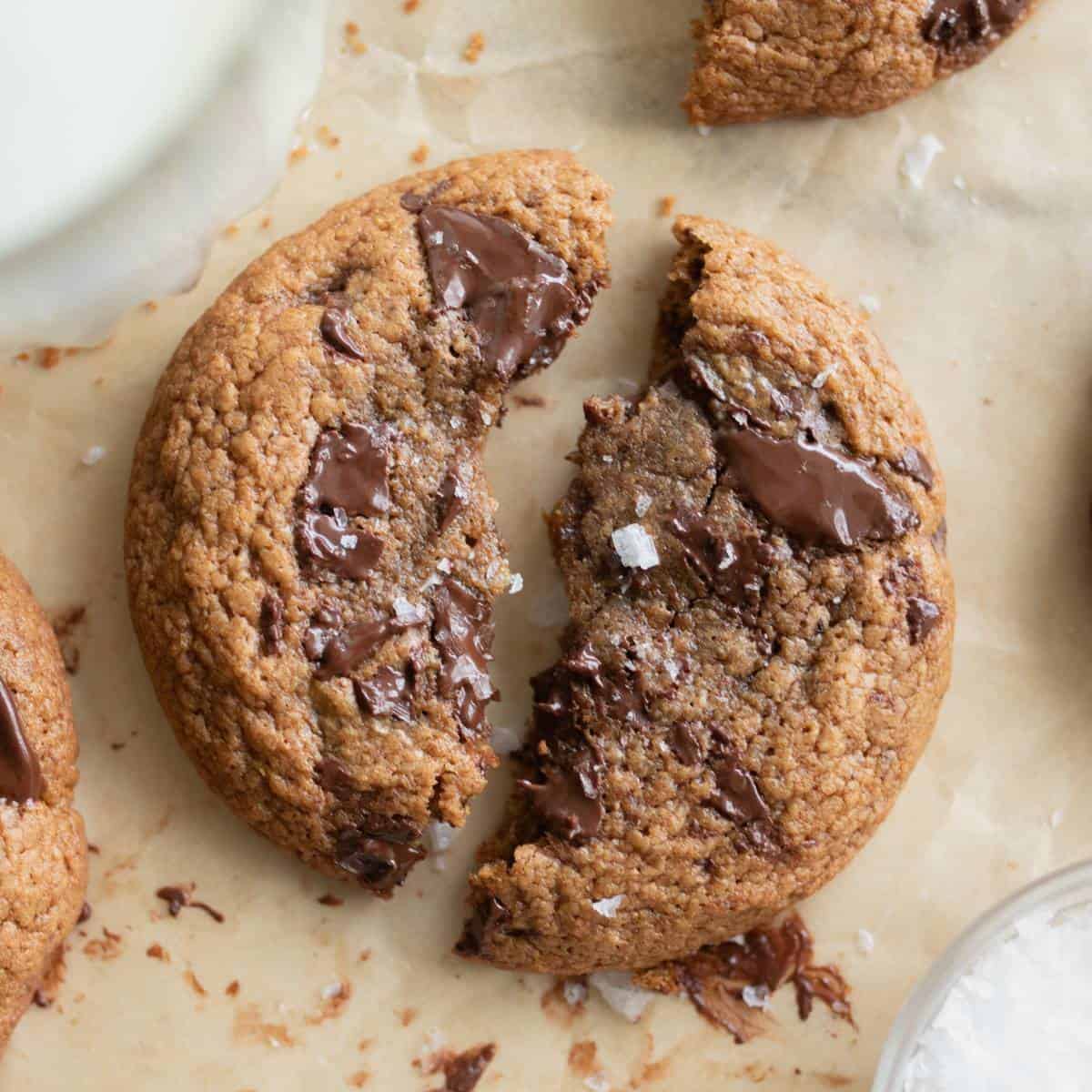 A broken in two spelt chocolate cookie has melting chocolate chunks on top.