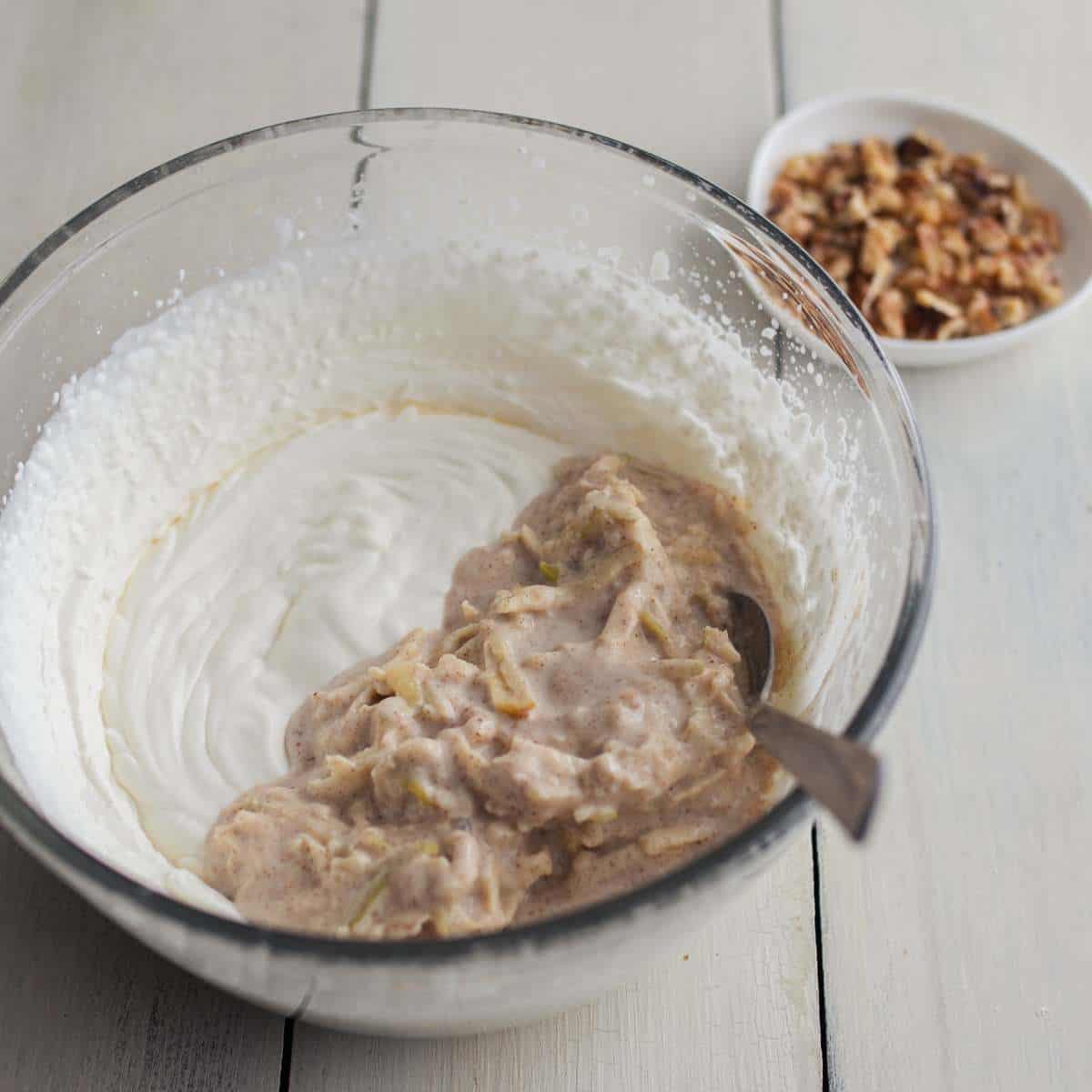 Greek yogurt mixture sitting on top of whipping cream in a clear bowl, ready to be mixed together.