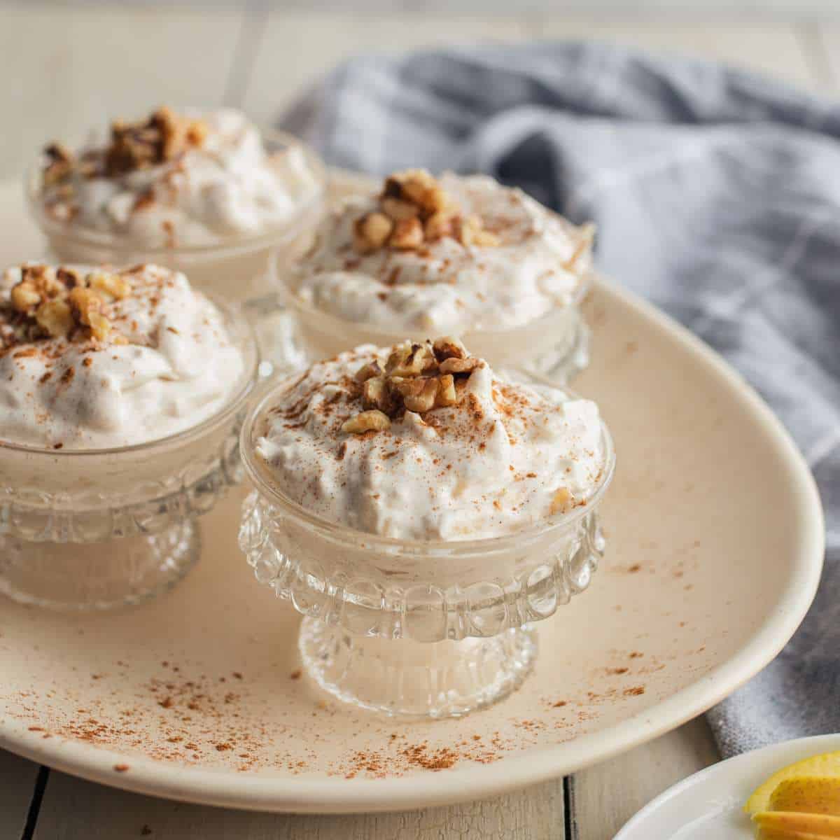 Four small dessert bowls of apple mousse on a plate garnished with cinnamon and chopped walnut.