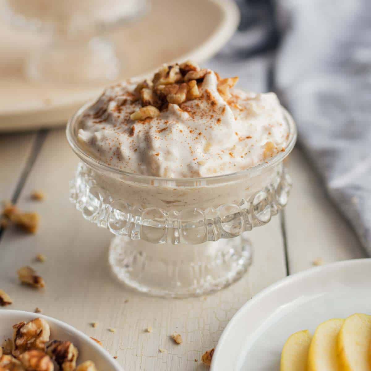 Apple Mousse topped with chopped walnut and cinnamon in an elegant glass dessert dish.