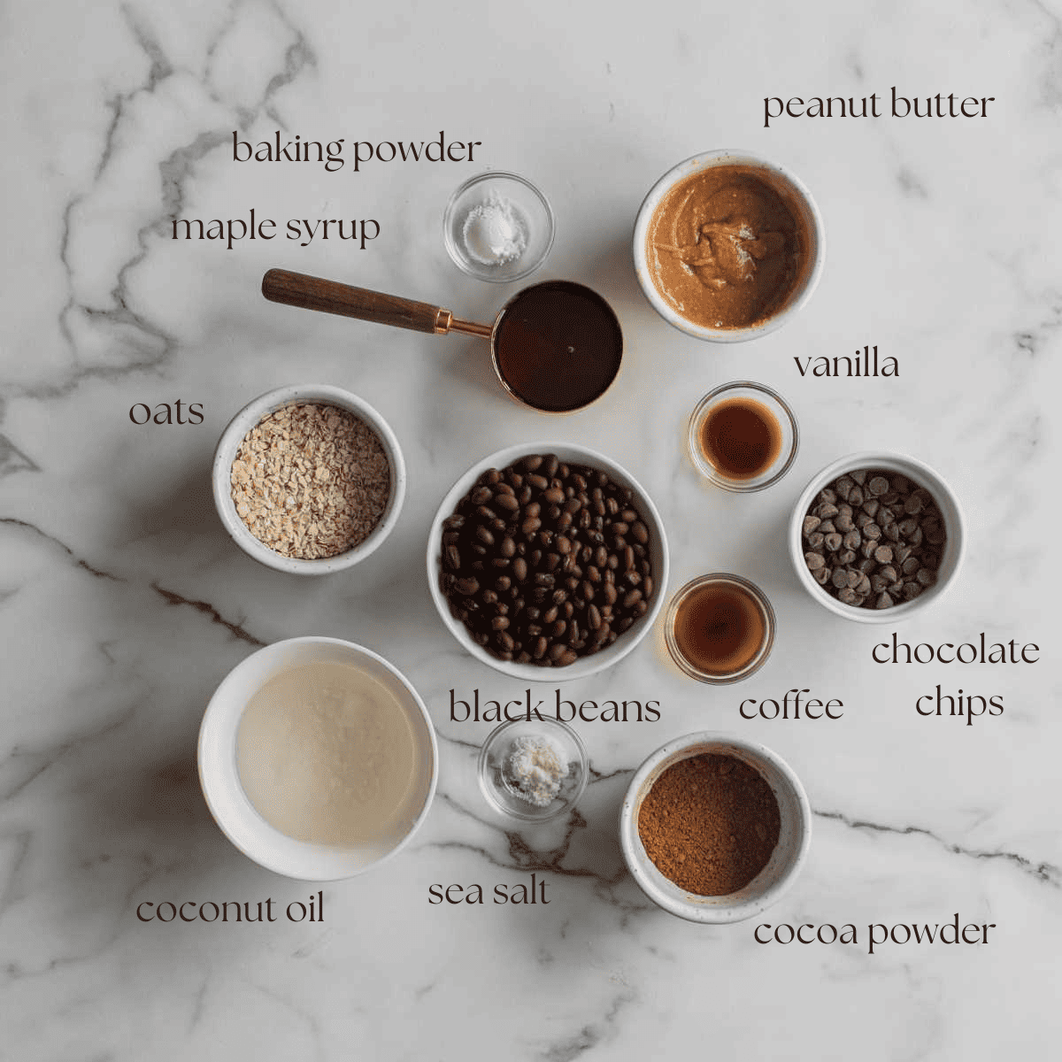 Ingredients to make peanut butter black bean brownies in pinch bowls, measuring cups and mixing bowls on a marble counter top.