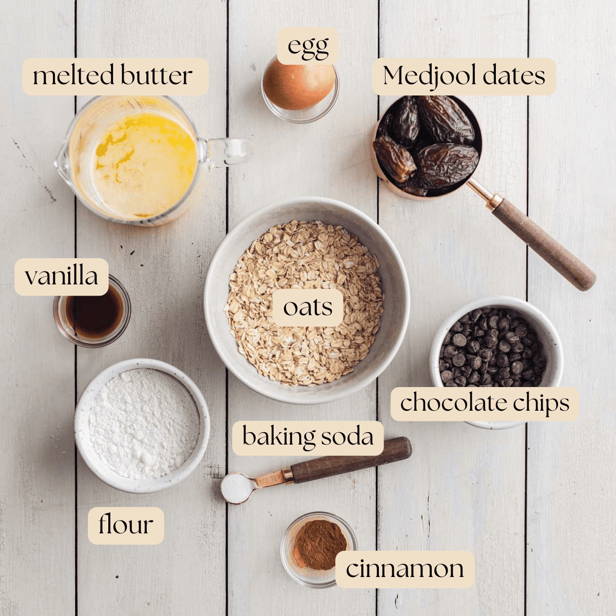 All ingredients to make date sweetened chocolate chip cookies in mixing bowls, pinch bowls and measuring cups on a wooden table.