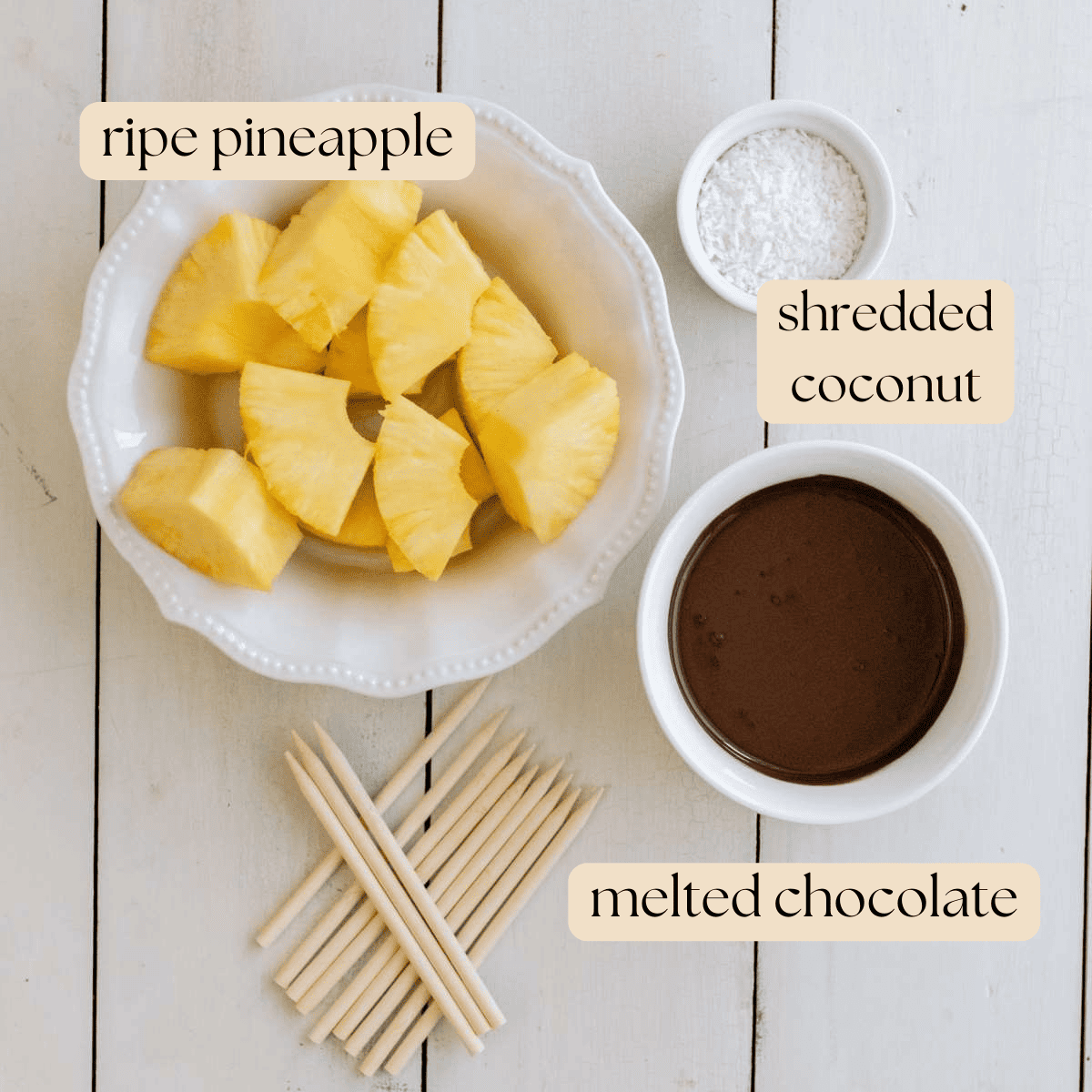 Ingredients for chocolate covered pineapple in bowls and laid out on a wooden board.