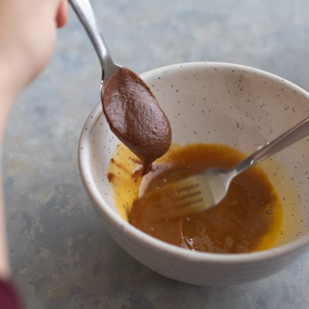 Slowly adding chocolate mixture into a mixing bowl of whisked egg yolks with a spoon.