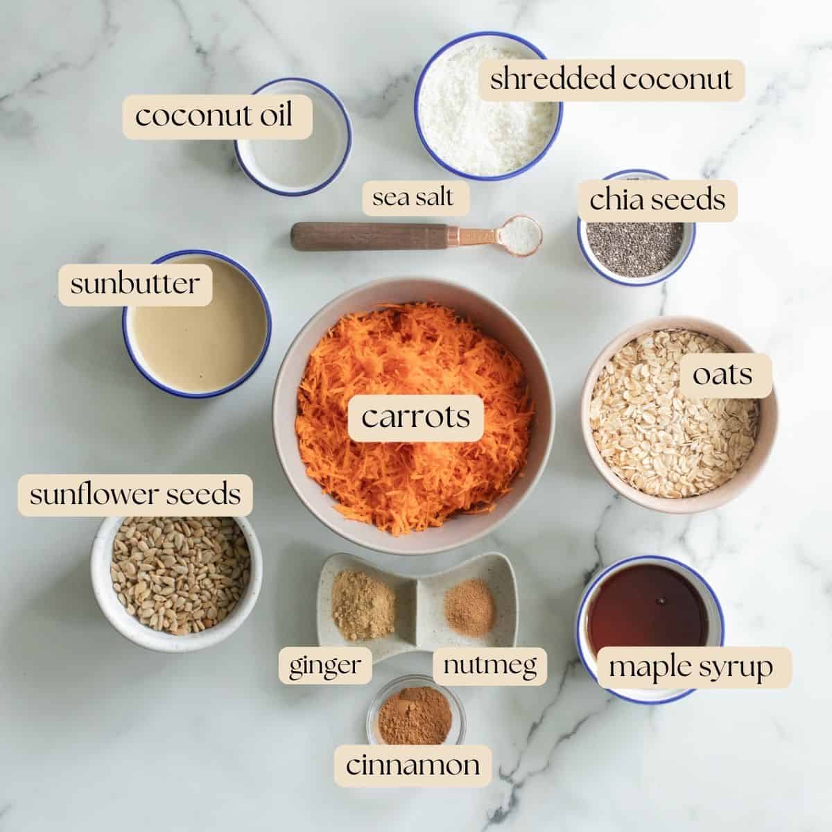 The 12 ingredients necessary to make carrot cake energy balls in pinch bowls, measuring cups and mixing bowls on a countertop.