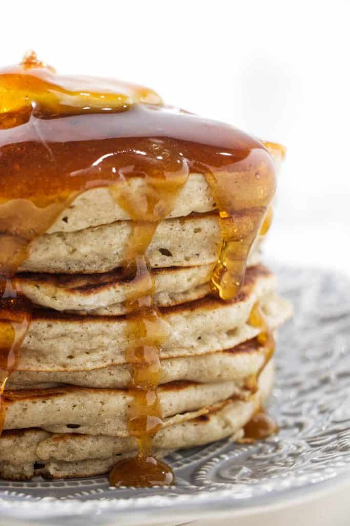 Seven barley pancakes stacked on a plate with syrup and butter on top.