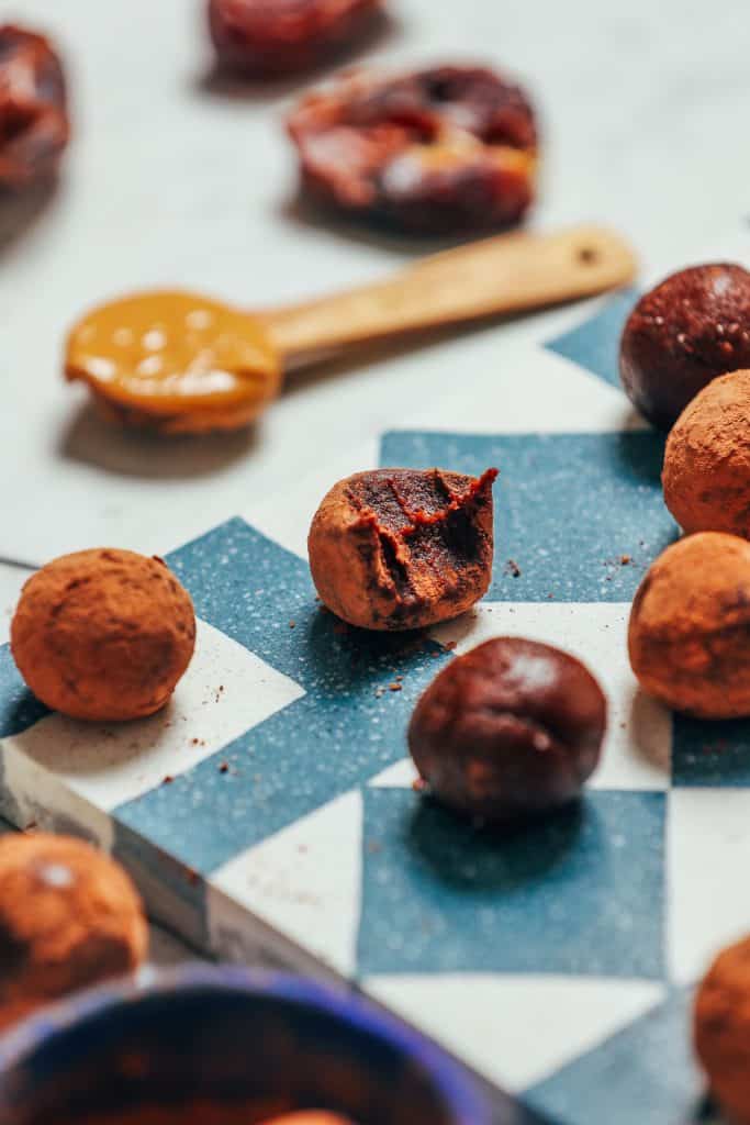 Chocolate truffles scattered on a table cloth around an ornate, wooden spoon.