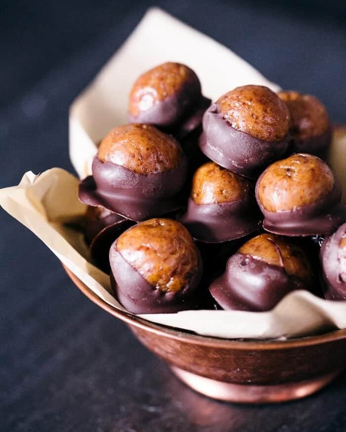 Peanut butter balls dipped in chocolate in a lined wooden bowl.