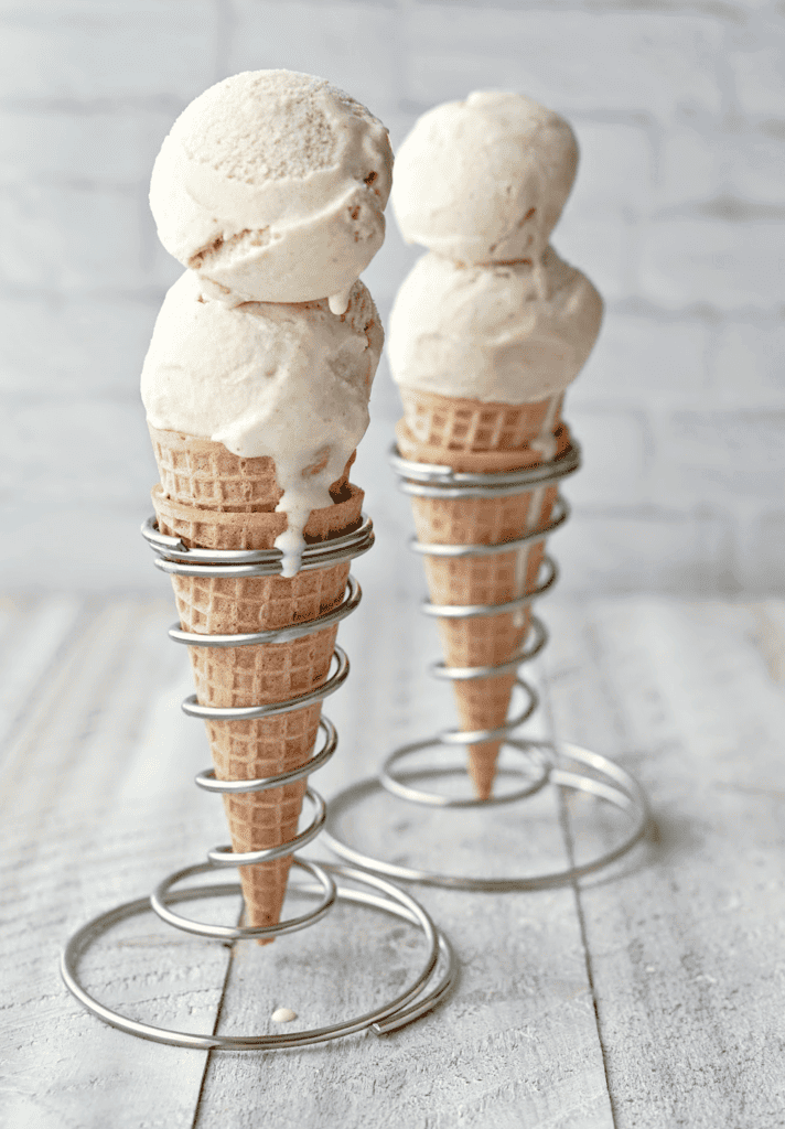Two scoops of ice cream in a double waffle cone standing up in a spiral, wire cone holder with another behind it.