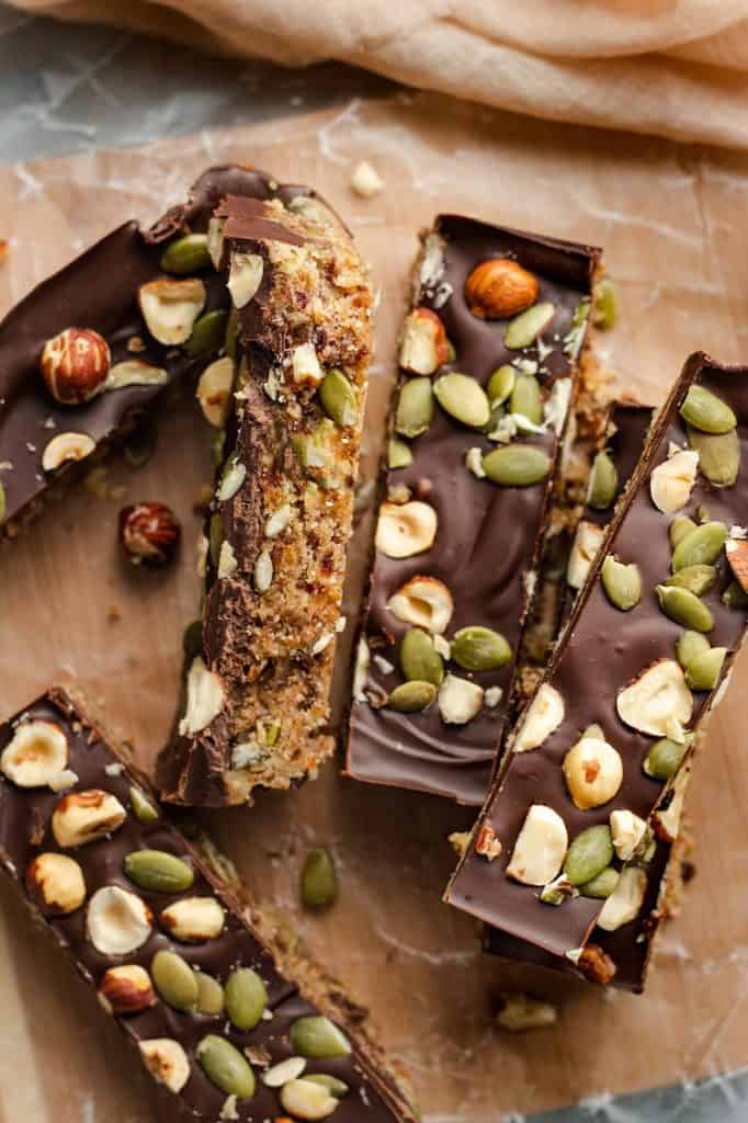 Four date nut bars on a cutting board with nuts embedded in chocolate on top.