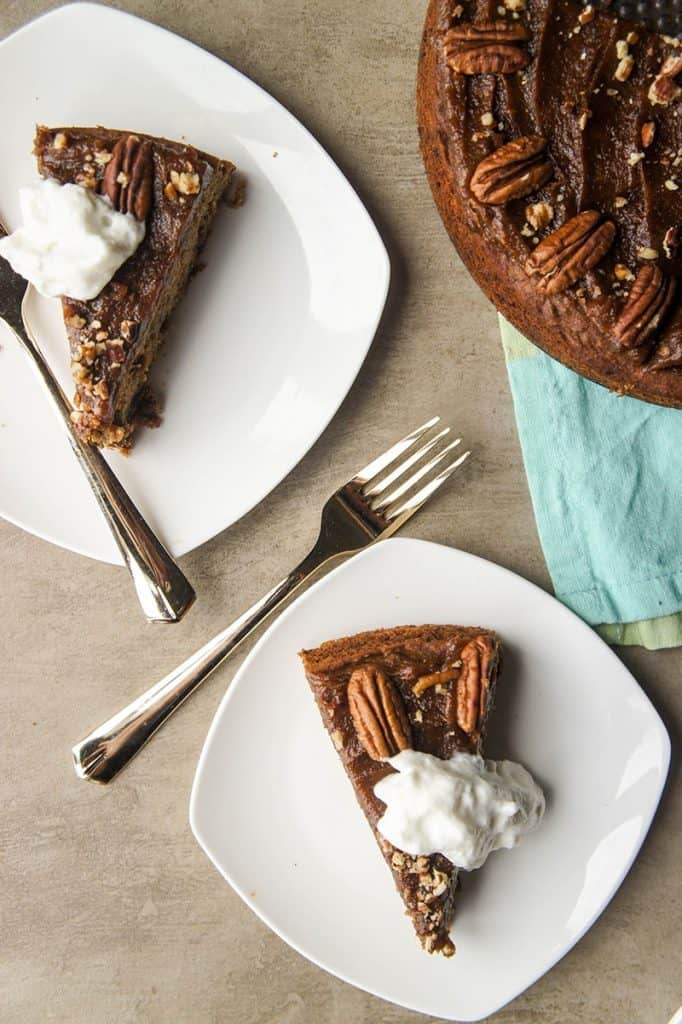 Two plated date pudding cake slices with whipping cream on top of the full cake off to the side.