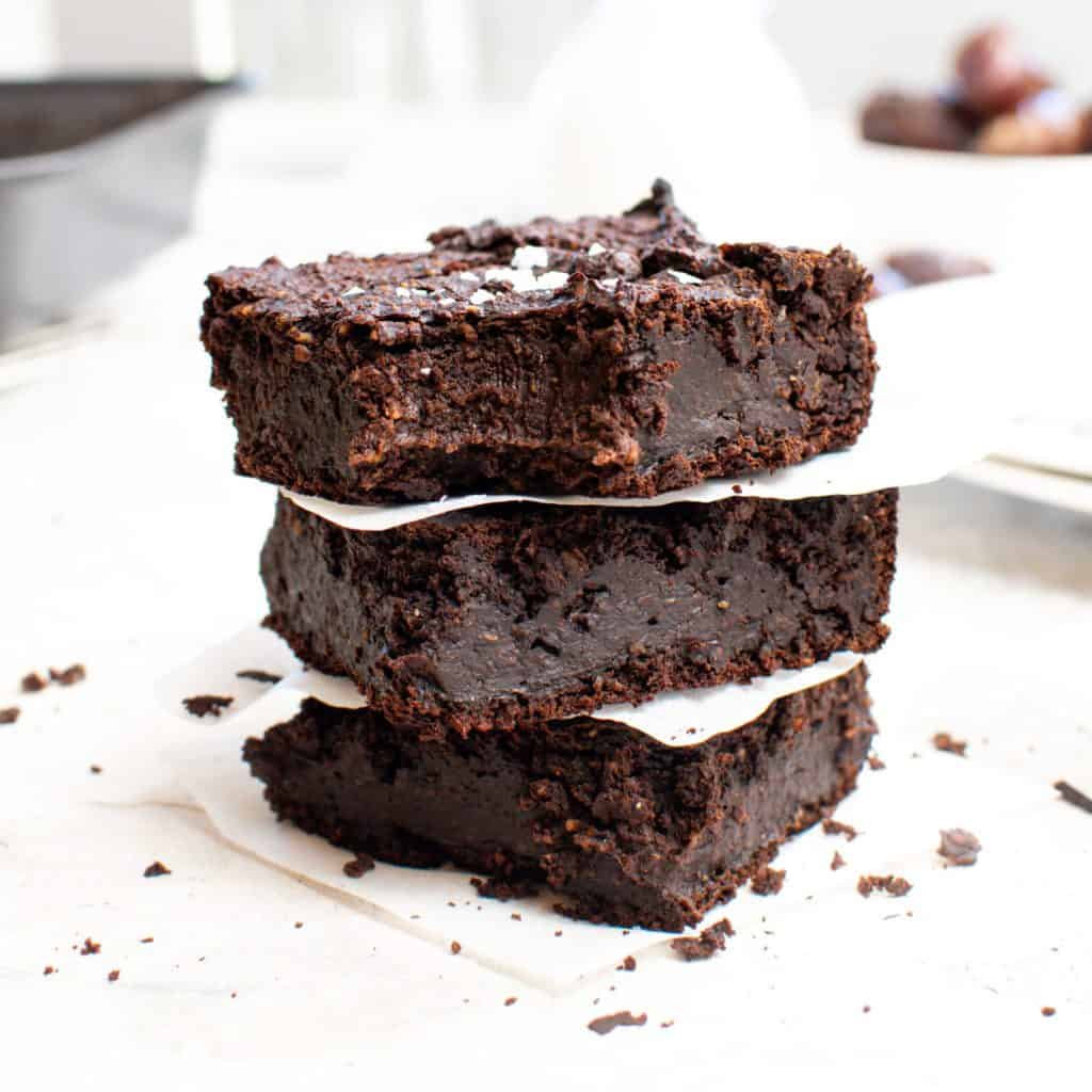 Three stacked date brownies with parchment paper between each and a bite taken out of the top one.