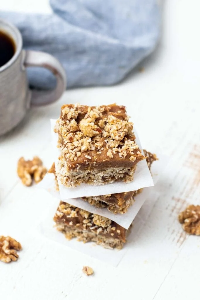 Three stacked walnut bars with walnut crumble on top and parchment paper between each one on a staged tabletop.
