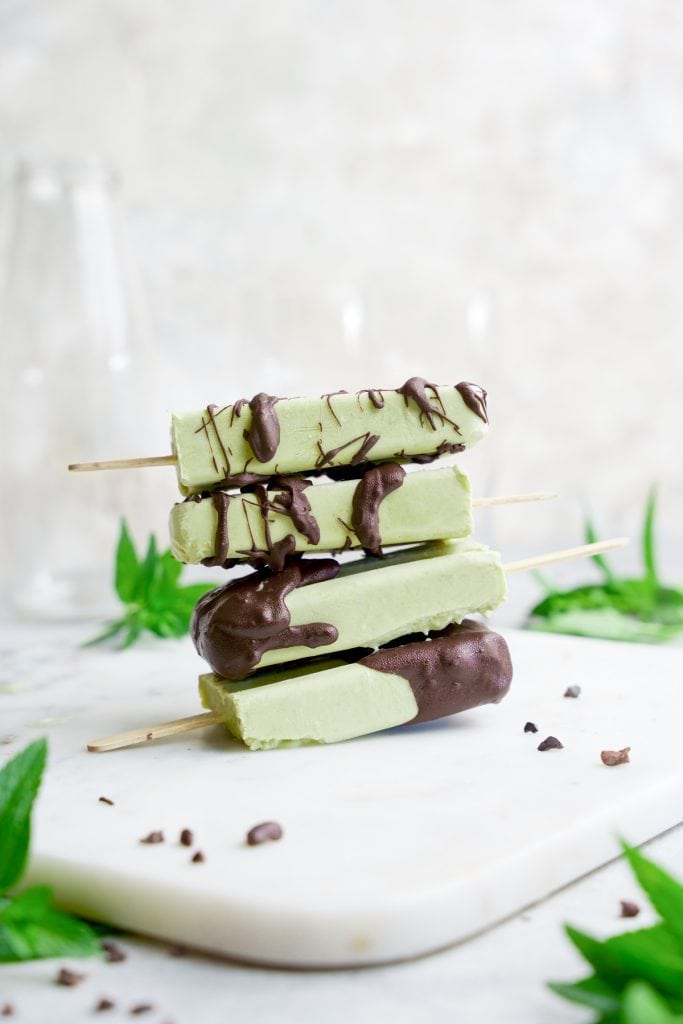 Four stacked matcha popsicles with chocolate drizzle on a white, staged table.