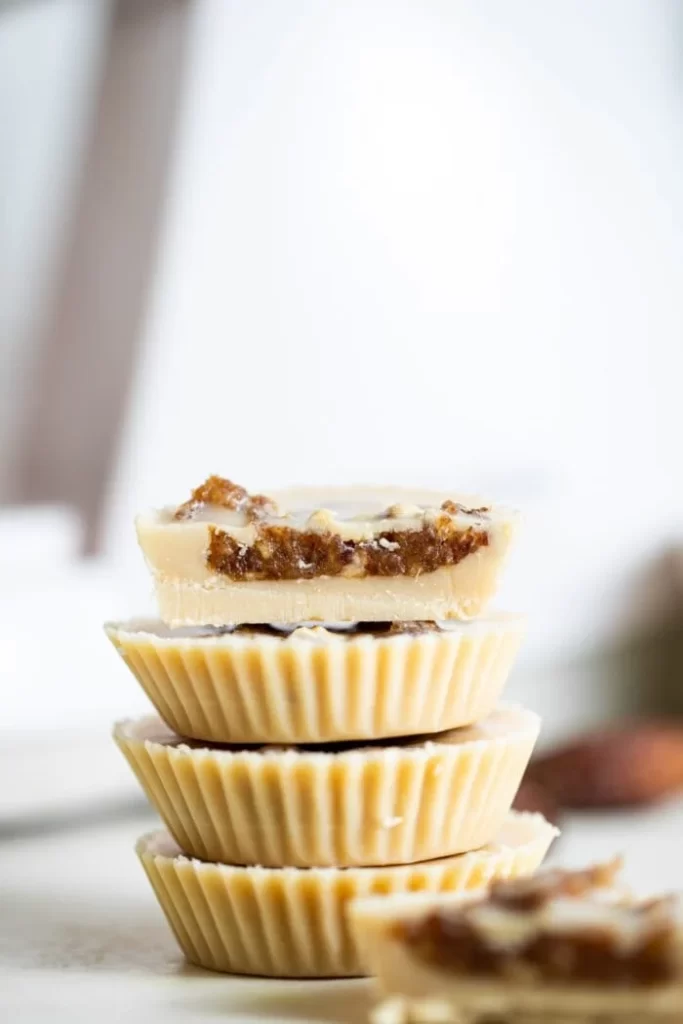 Four stacked tahini cups with a bite out of the top one showing their thin profile and date filled center.