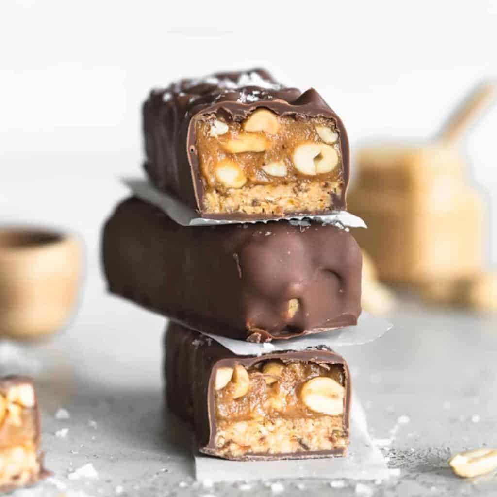 Three stacked vegan snickers bars with parchment paper between each. two are cut to show the texture inside.