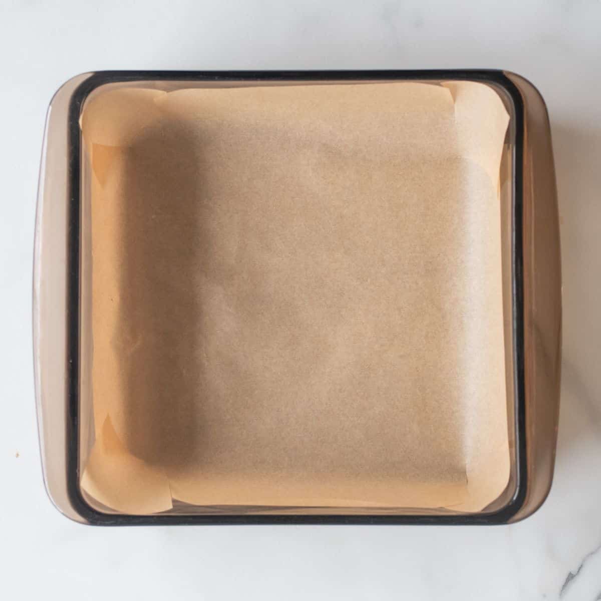 An overhead view of an 8-inch baking dish lined with parchment paper.
