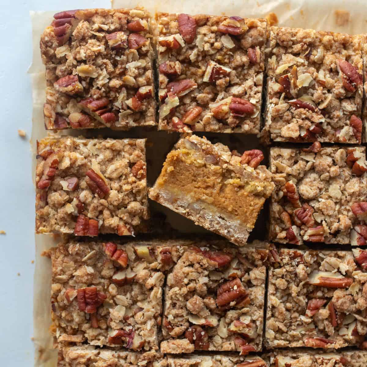Cut pumpkin pecan bars on parchment paper focused on one turned sideways showing the layers of the bar.