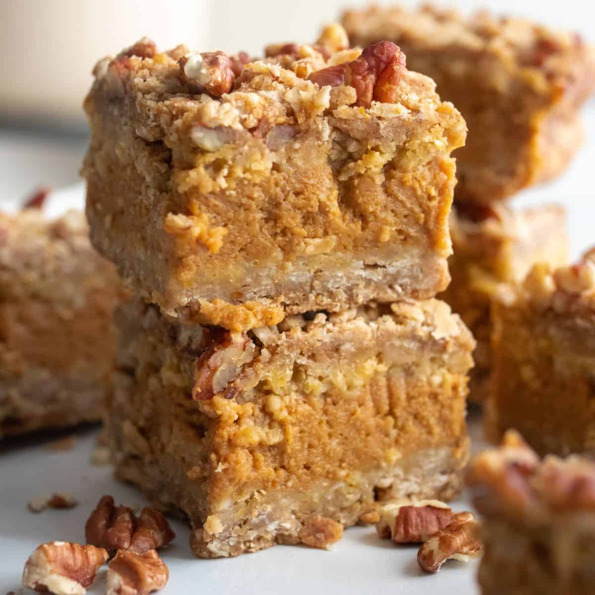 Two pumpkin pecan bars stacked on top of each other with other bars and nuts around.