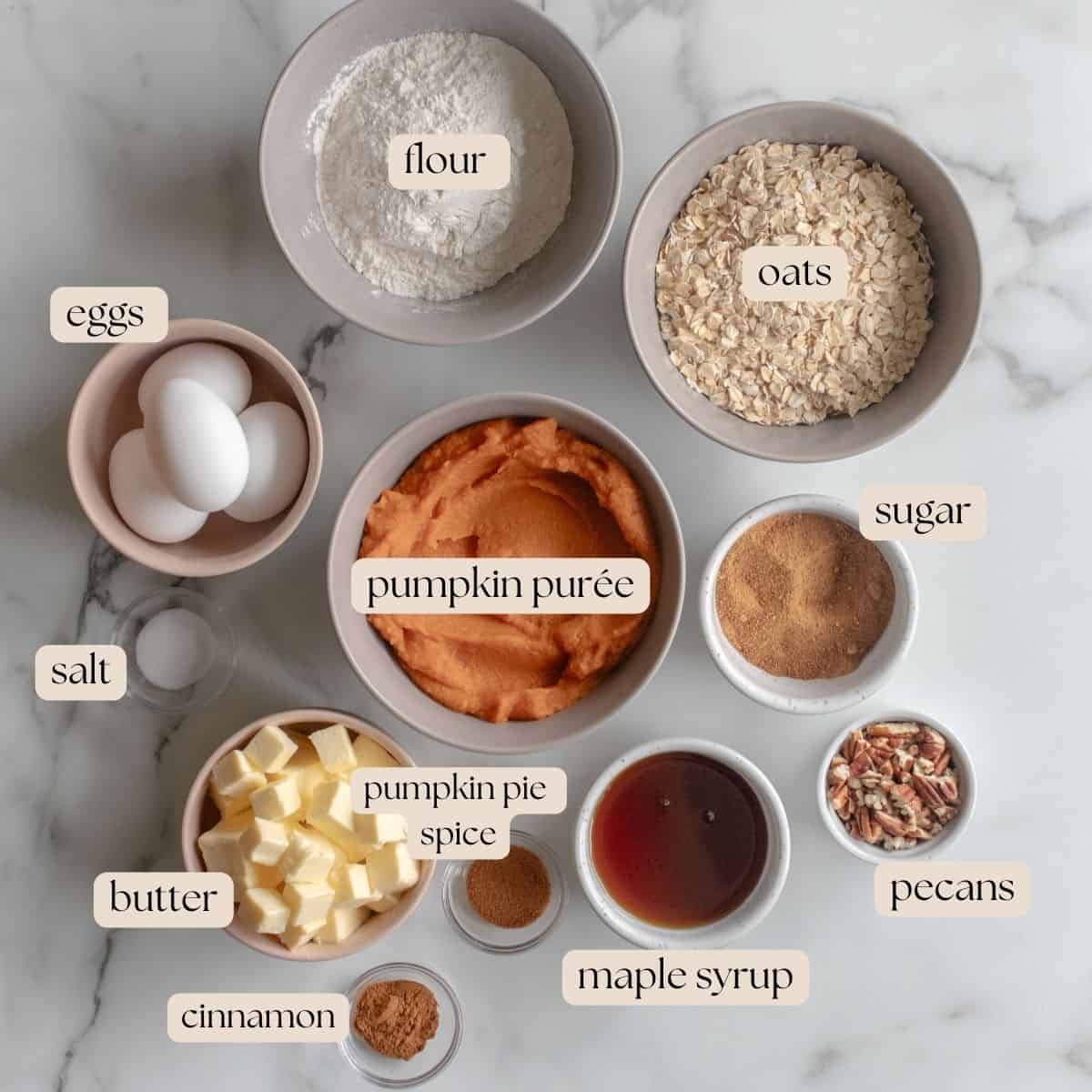 Ingredients to make pumpkin pecan bars in bowls and pinch bowls on a marble countertop.