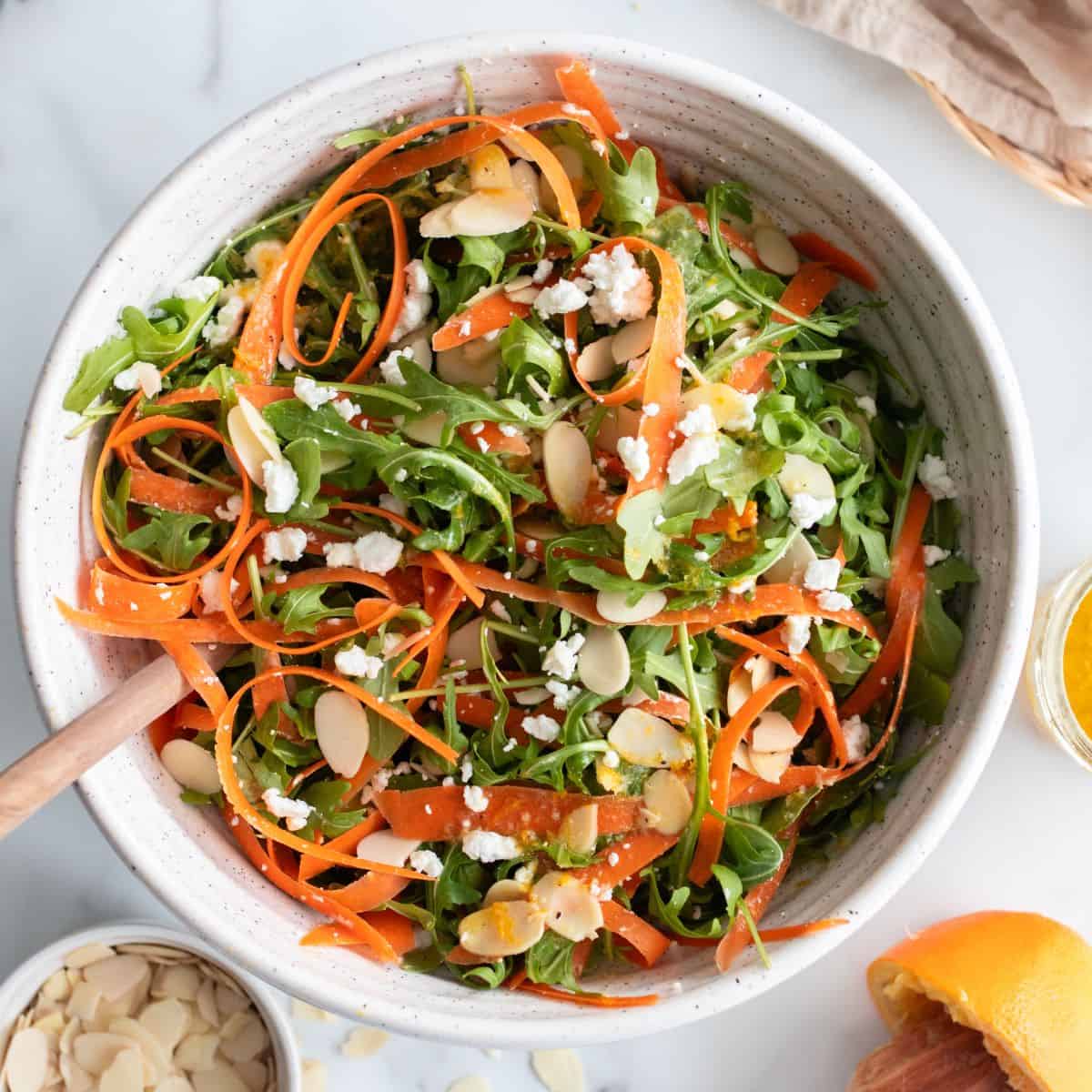 Overhead view of a wooden spoon inside a tossed ribbon carrot salad.