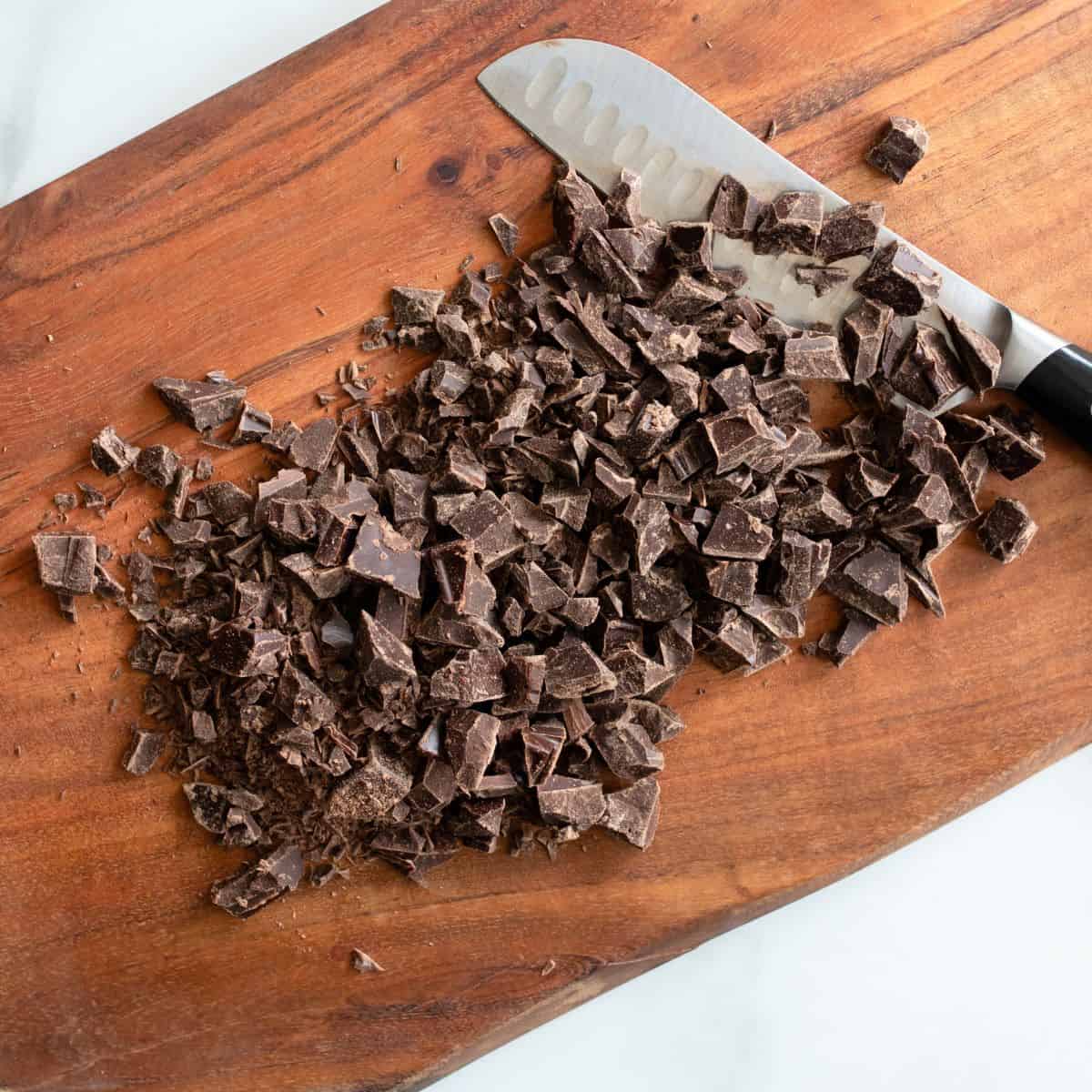 Chopped semi sweet baker's chocolate on a cutting board with a large knife on top.