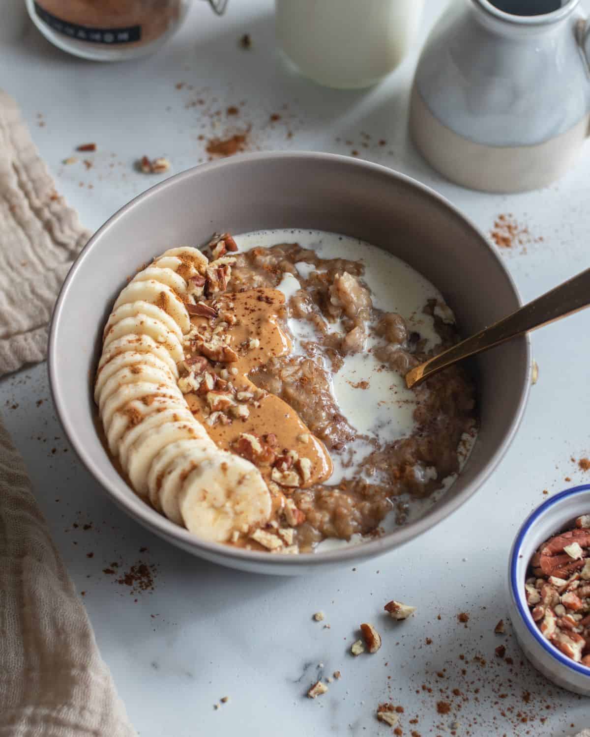 Bowl of date oatmeal with banana, pecan and cream topping.