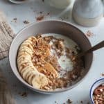 Sliced banana, peanut butter and walnuts topping date oatmeal on a staged countertop.