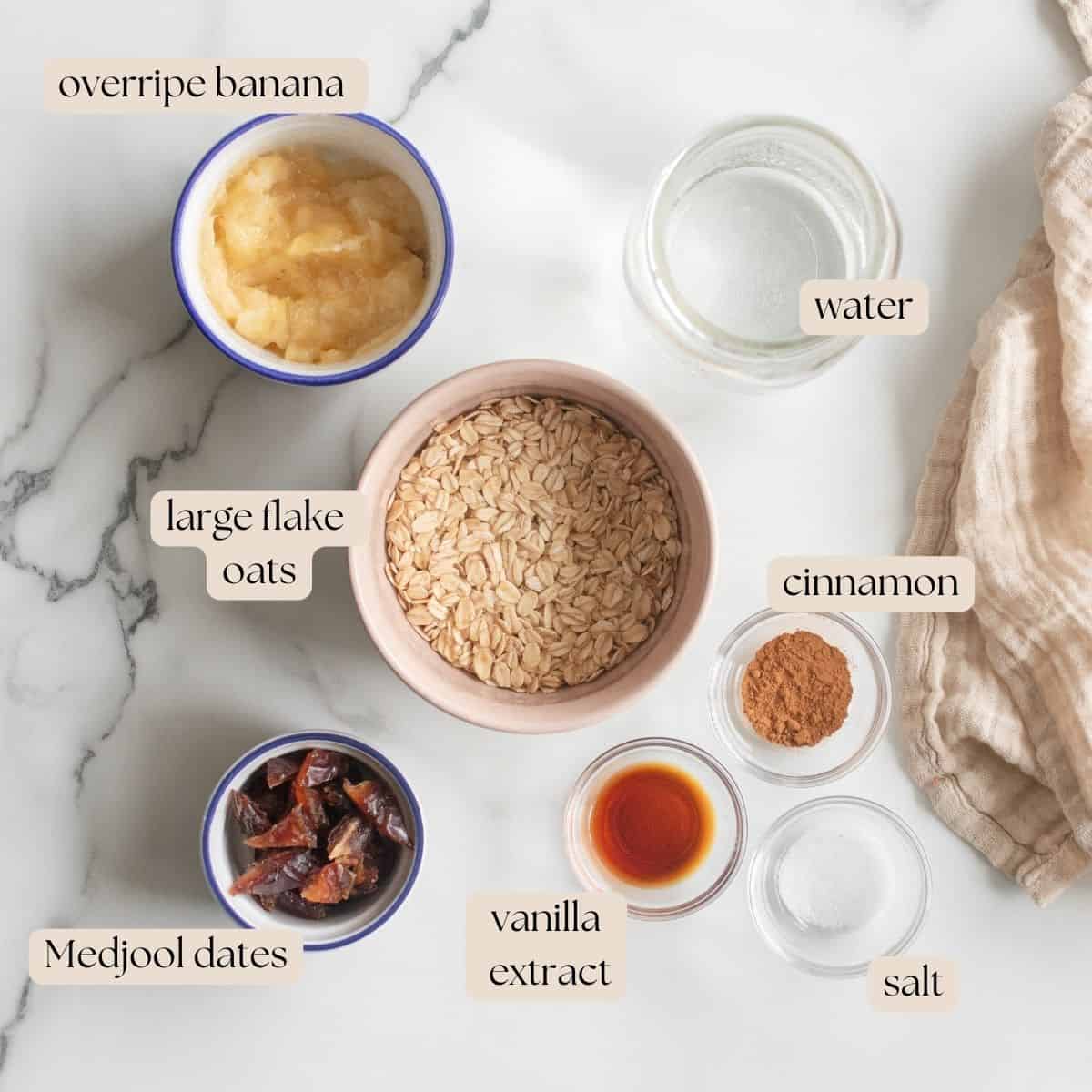 Ingredients to make banana date oatmeal in mixing bowls and pinch bowls on a countertop.