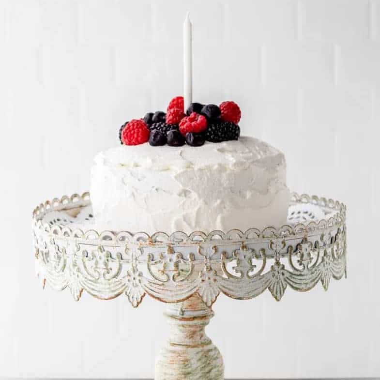 Icing covered baby smash cake with fresh fruit topping and a single birthday candle on an ornate cake plater.