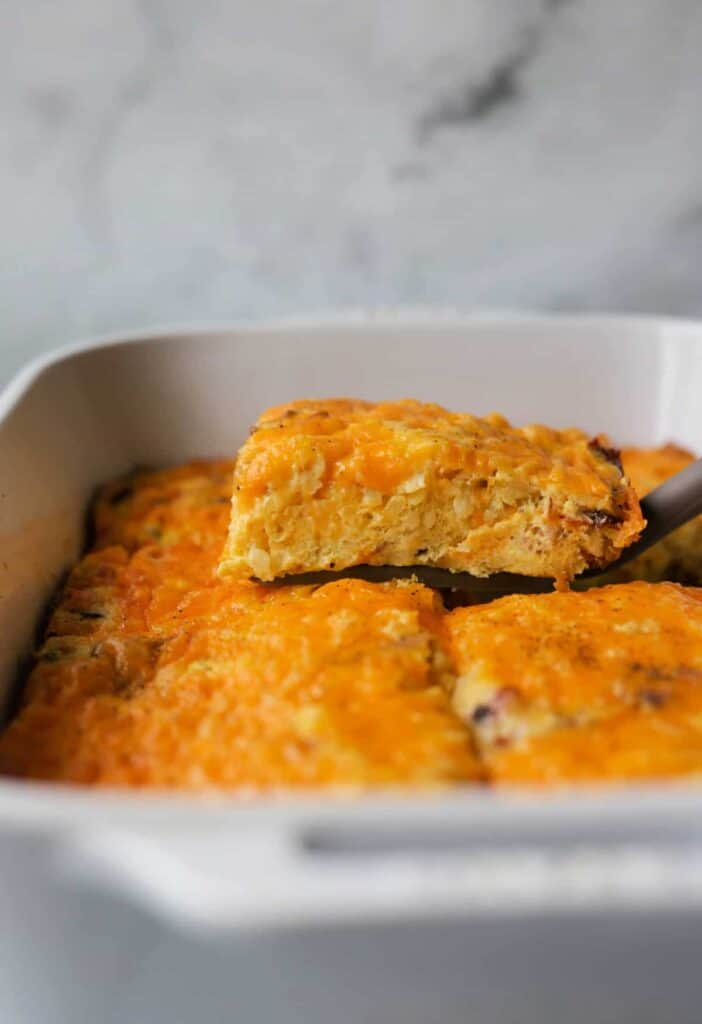 A piece of cottage cheese breakfast casserole coming out of a low, ceramic casserole dish on a spatula.