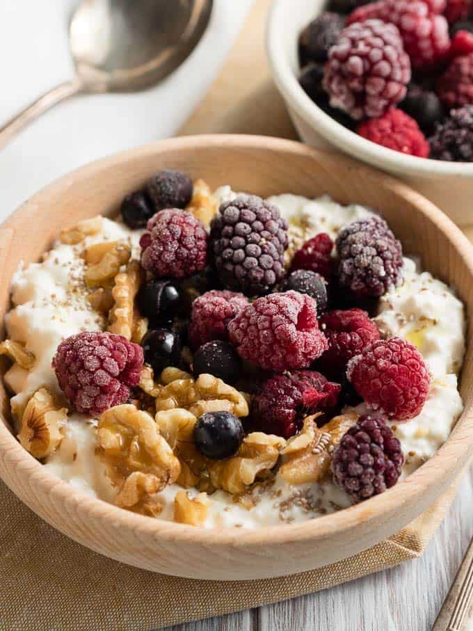 Blended cottage cheese with walnuts and fruit on top in a wooden bowl.