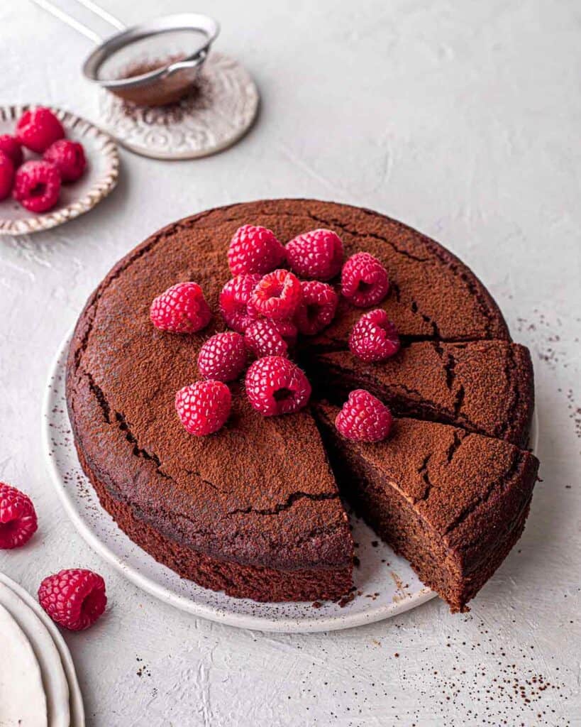 Flourless chocolate cake with raspberry topping with two pieces cut ready to serve.
