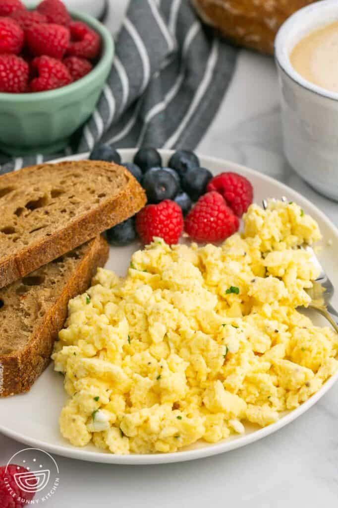 Scrambled eggs on a plate with toast and fresh blueberries and raspberries on a staged table.