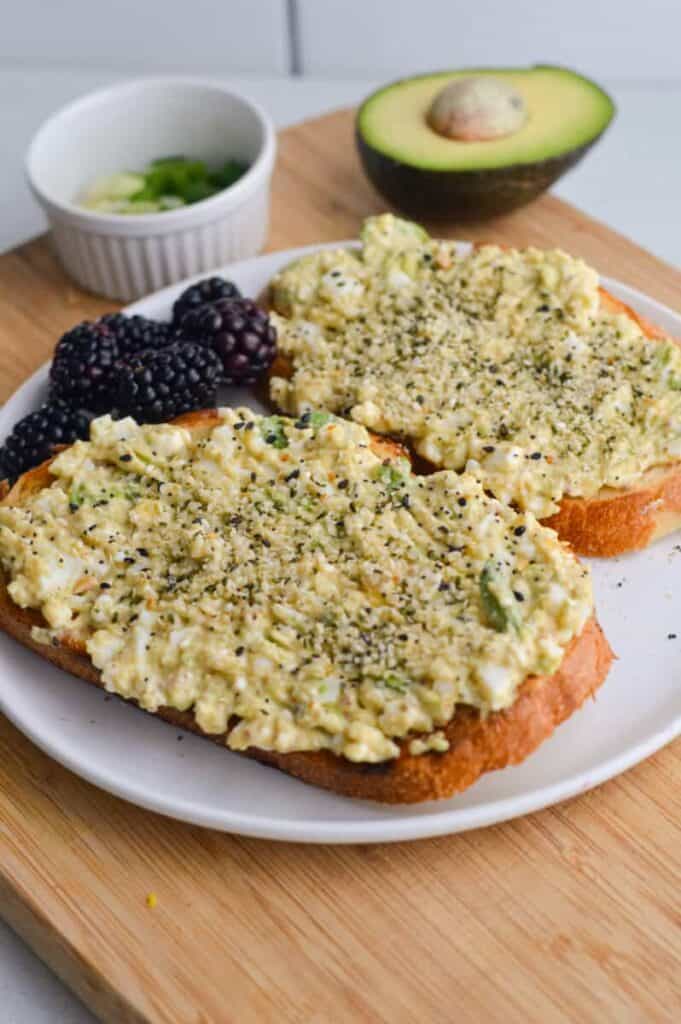 Open face sandwich with avocado cottage cheese spread on top, staged on a cutting board with a avocado half.