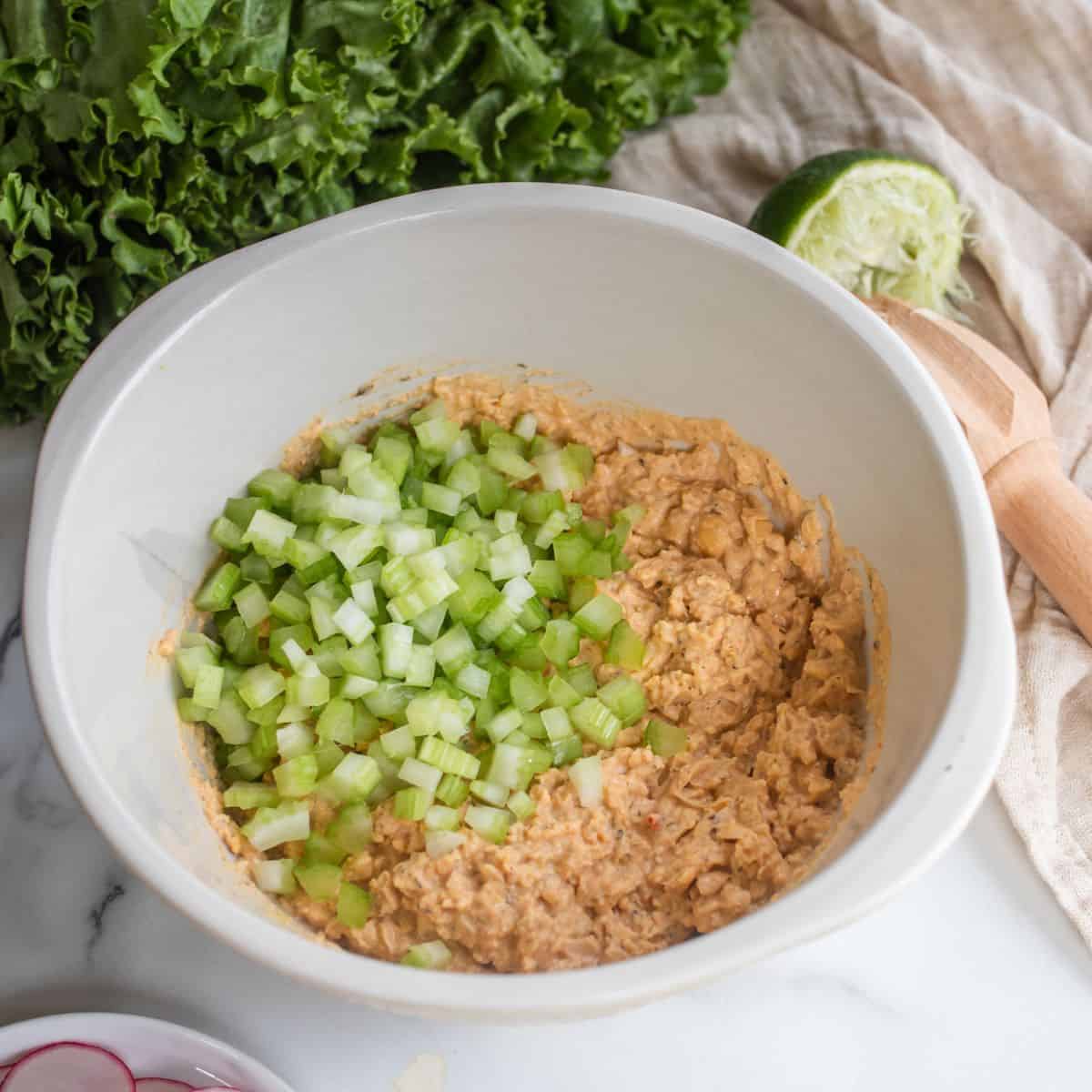 Chickpea mixture with cut celery on top in a mixing bowl.